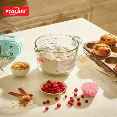 Kitchen countertop with flour in a measuring cup, raspberries, brown sugar, baking tools, and muffins cooling on a rack.
