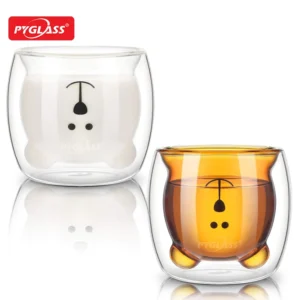 Two double-walled glass cups featuring adorable bear designs, one with milk and the other with tea. High-quality PYGLASS branding is visible.