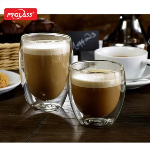 Two double-walled glass cups filled with coffee on a wooden table, accompanied by a white coffee cup and assorted bakery items.