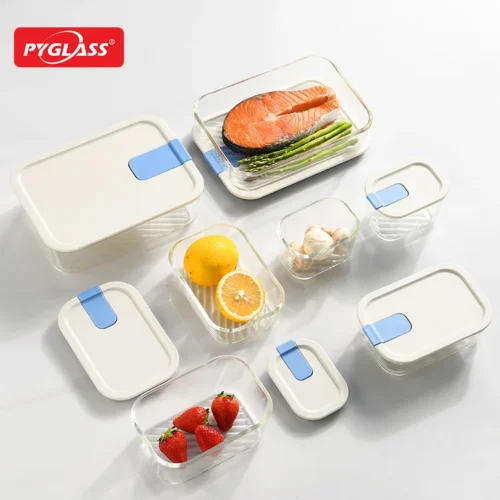 Set of glass food storage containers with white lids and blue accents containing various foods like salmon, lemons, and strawberries.