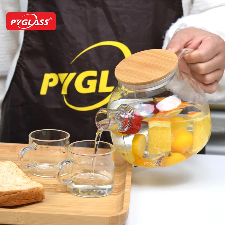 Hand pouring fruit-infused water from a glass pitcher into a small glass on a wooden tray with additional glass and a slice of bread.