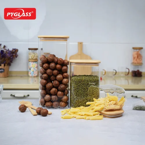 Glass food storage jars filled with macadamia nuts, green beans, and pasta on a kitchen countertop with wooden lids.
