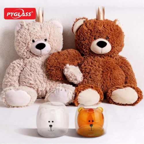 Two plush teddy bears wearing small crowns with two glass cups in front, featuring bear face designs.
